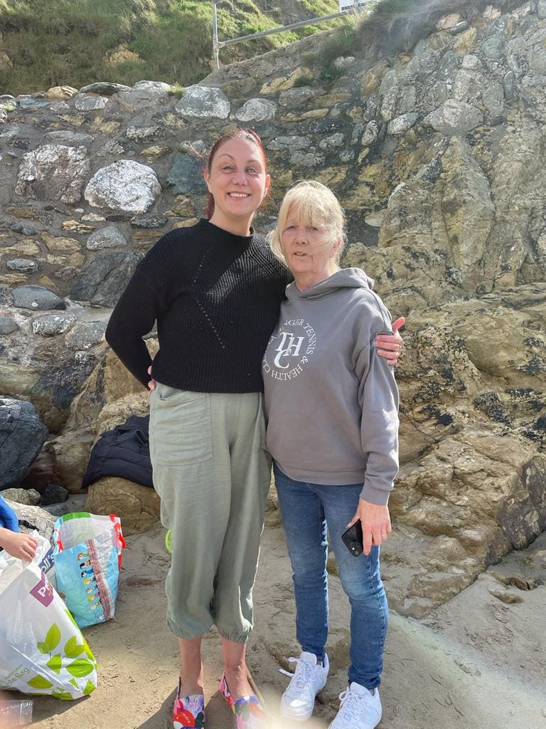 Holiday photo. Me and my Mum linking shoulders standing on the beach in sunshine. 