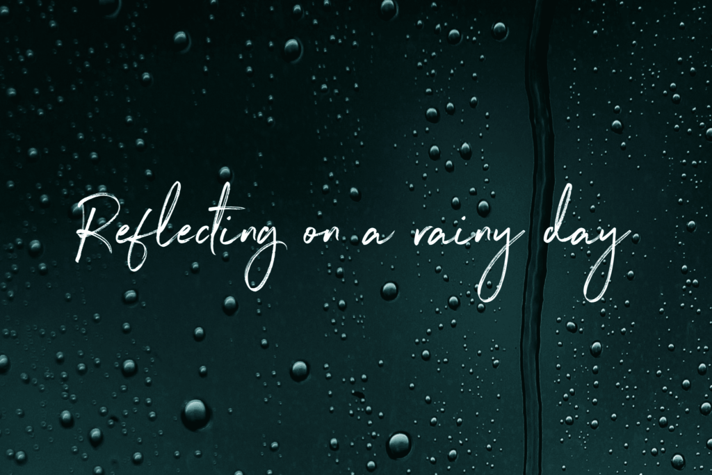 Black/green background with rain drops, like on a window pane. White text reads Reflecting on a rainy day on handwriting font. 