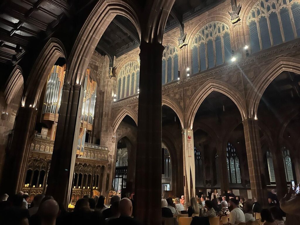 Image of inside Manchester Cathedral. Dark gothic pillars, candle lit.