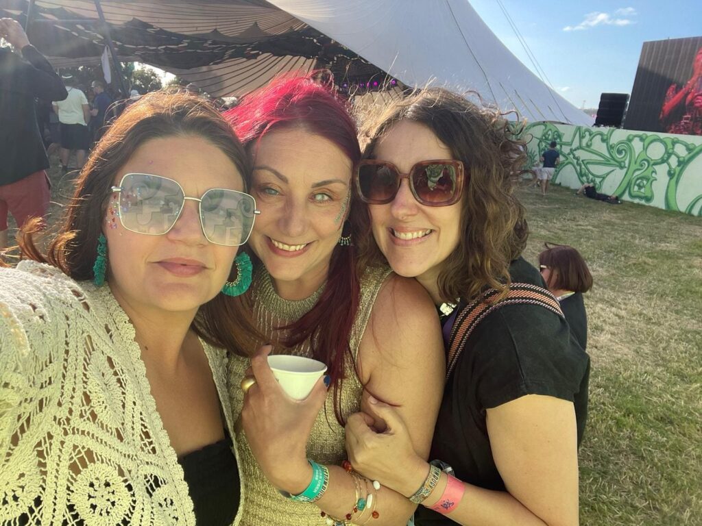 Nina with her sister and friend at Glastonbury. Huddled together wearing sunglasses. 