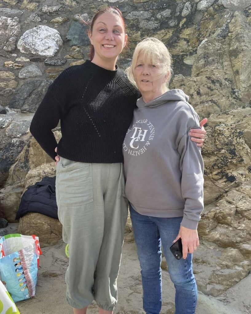 Nina and her mum on a beach with arms around each other. Holiday smiles in place. 