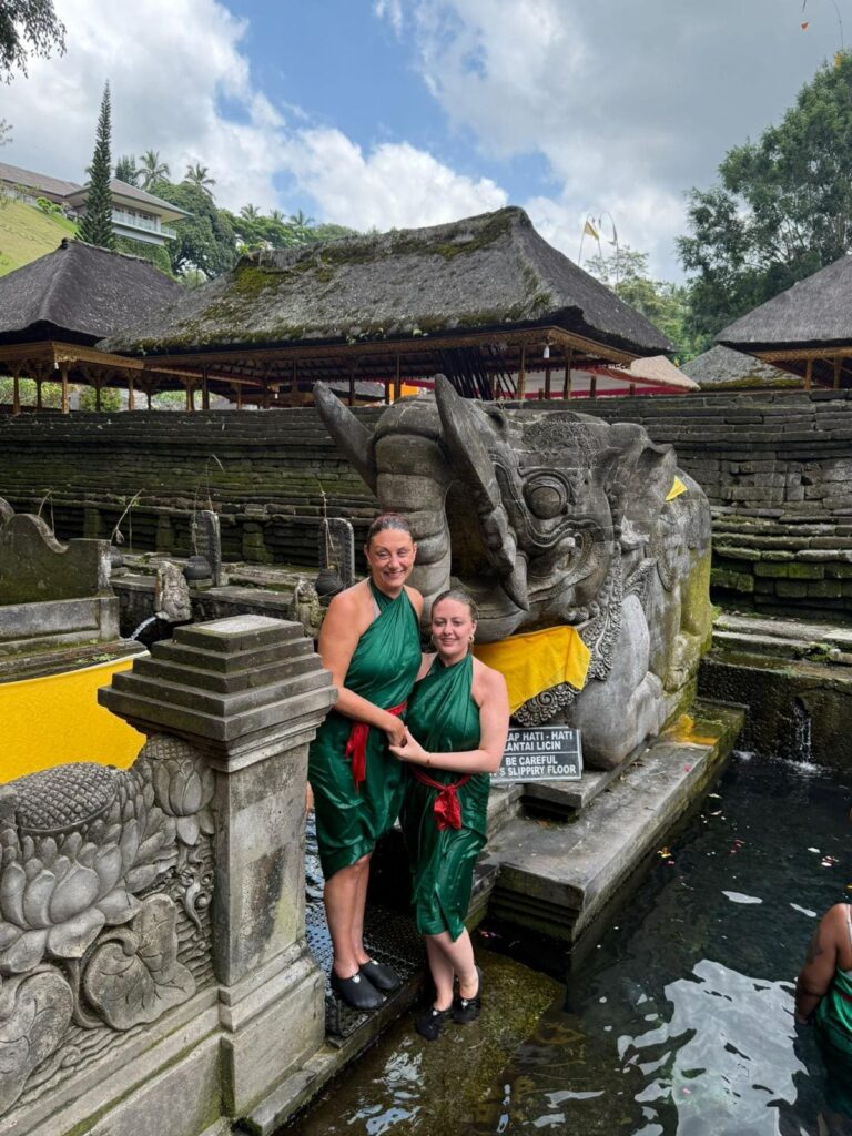 Nina and her sister Sam wearing green robes with red waist bands standing next to the healing waters.